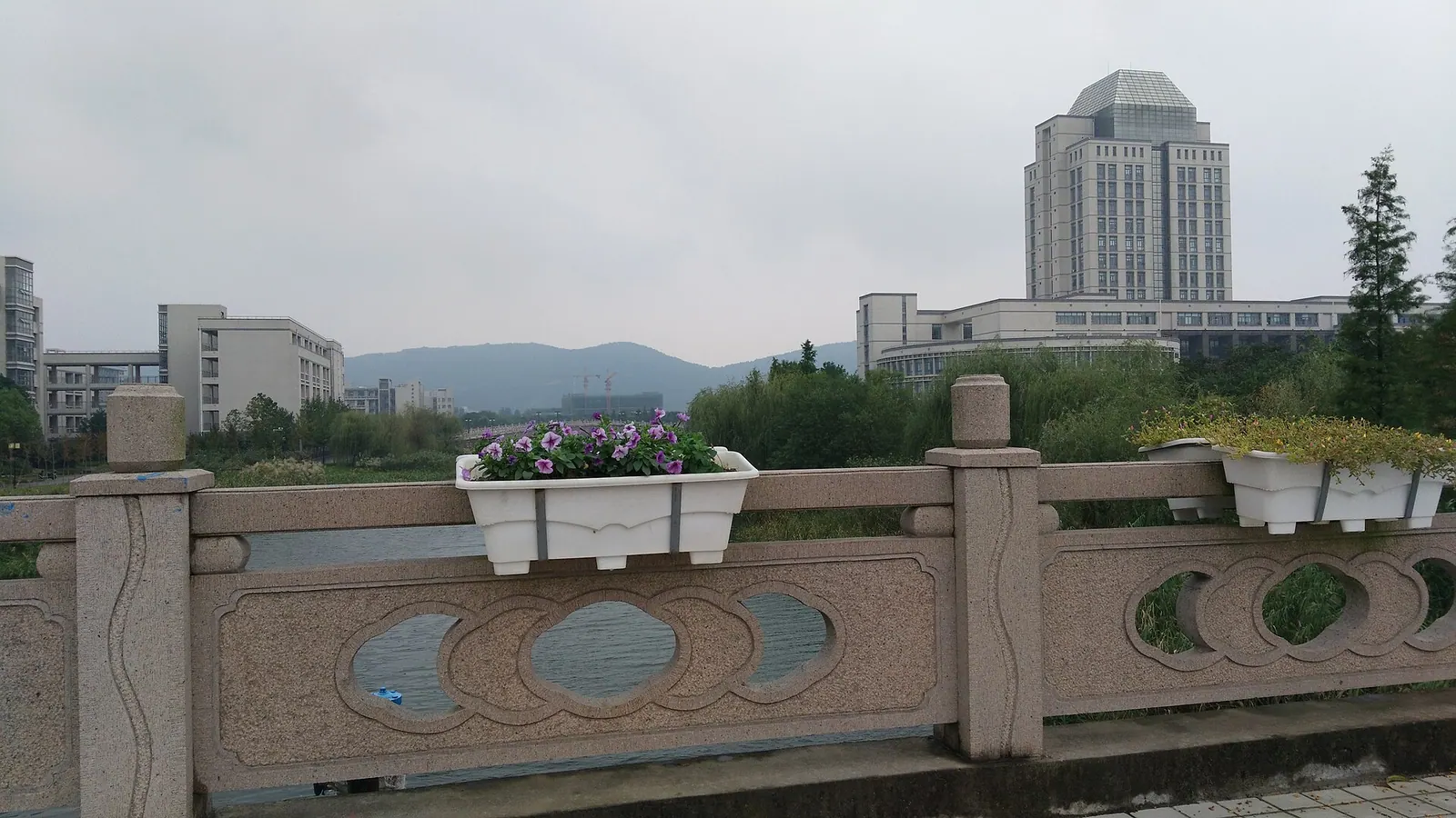 Cầu đá có chậu hoa, mặt nước và các tòa nhà trong khuôn viên Đại học Giang Nam.