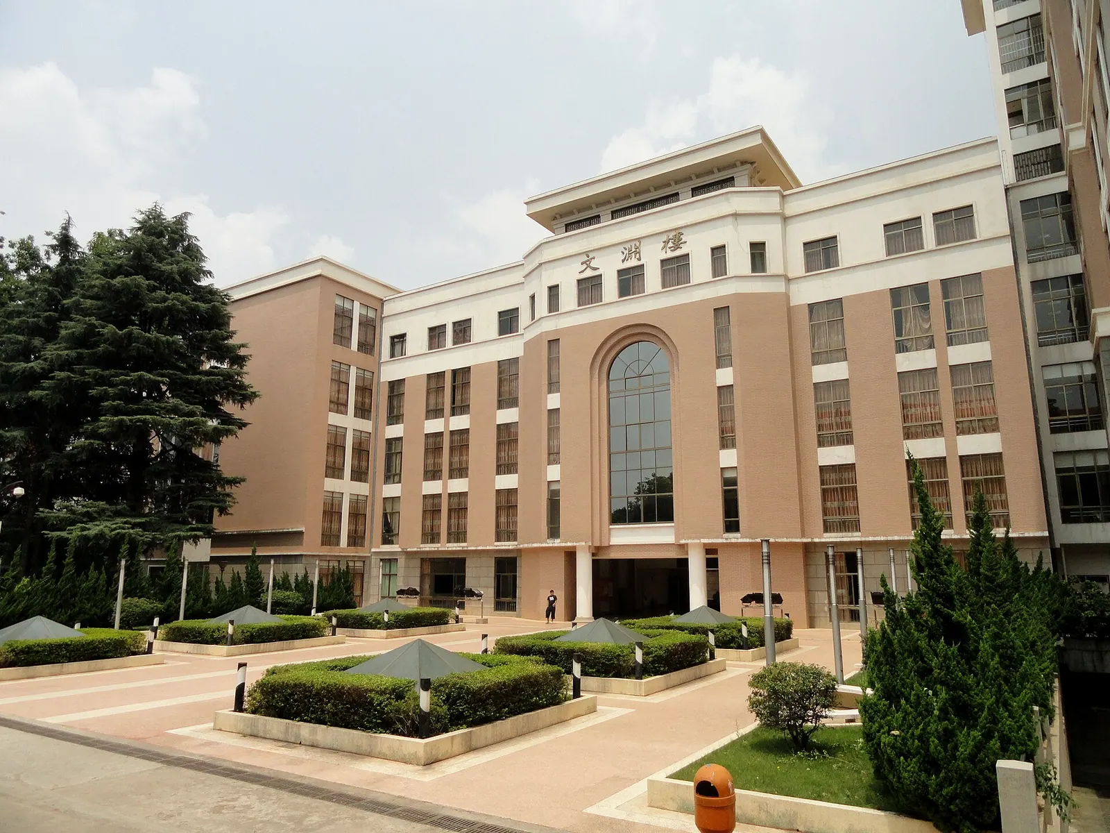 Tòa Wenyuan của Đại học Vân Nam với cửa sổ vòm cao, sân lát gạch và các bồn cây phía trước.