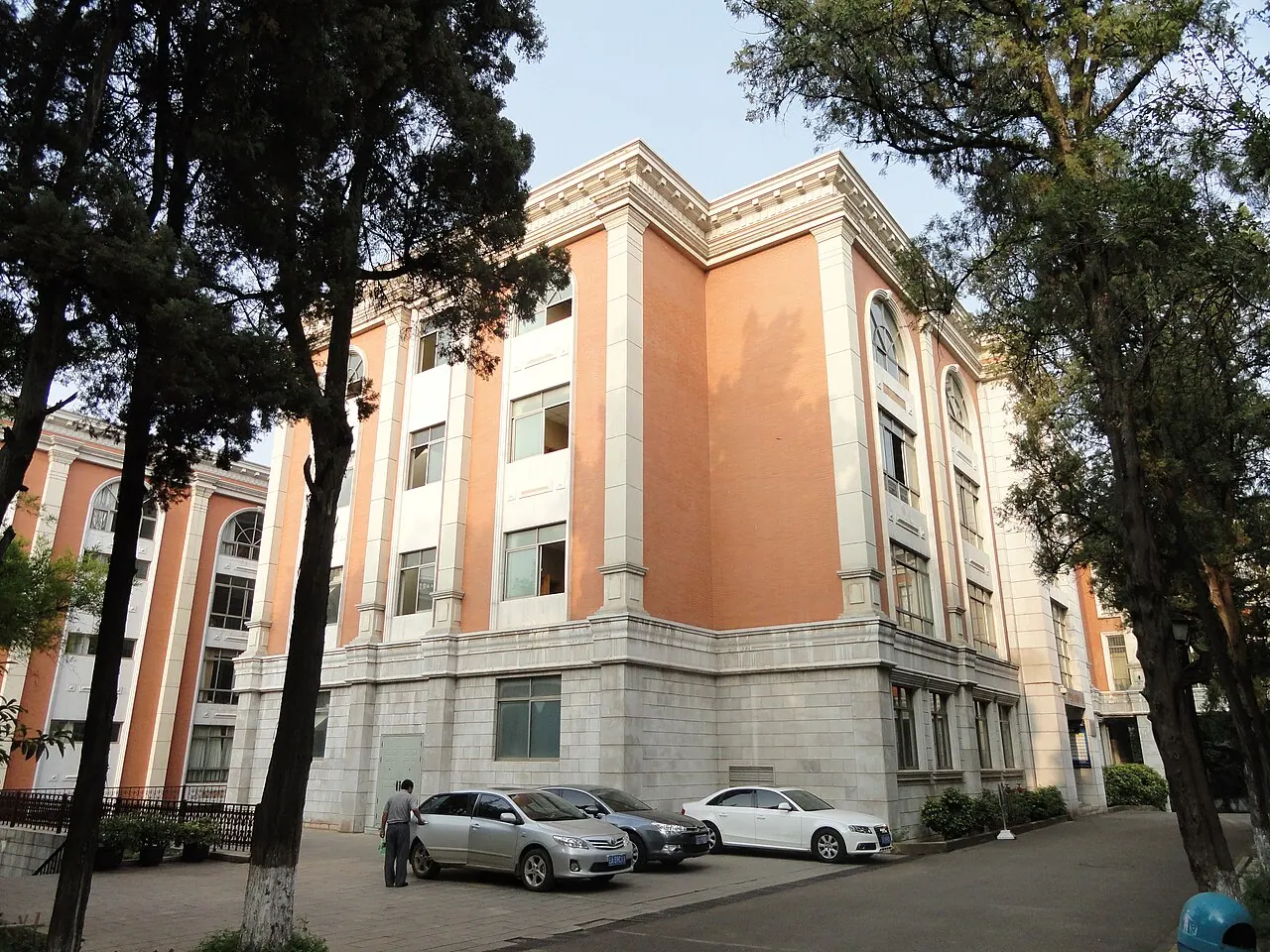 Tòa Wenjin màu cam nhạt với các ô cửa cao, phía trước có hàng cây tại Đại học Vân Nam.